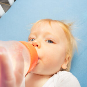 criança bem pequena de cabelo ruivo, tomando água na mamadeira