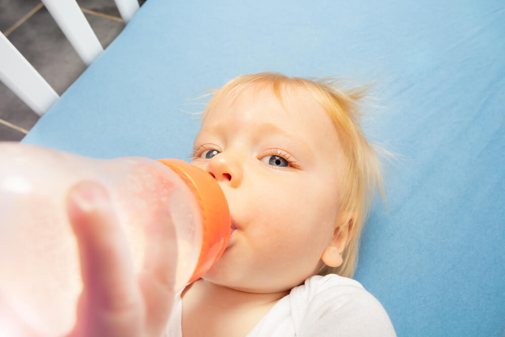 criança bem pequena de cabelo ruivo, tomando água na mamadeira